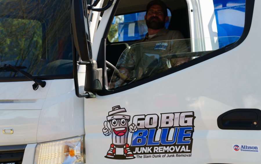 Front view of a dump truck cab with Go Big Blue Junk Removal worker getting out